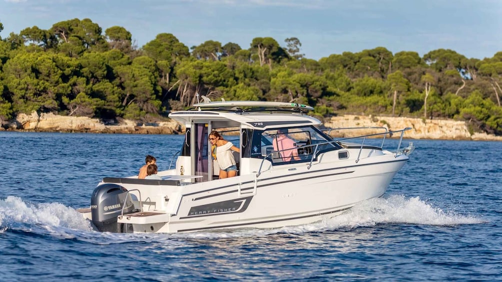 A white motorboat with a Yamaha outboard motor, named 'Merry Fisher,' moving through a body of water with a rocky shoreline and dense green trees in the background. 1