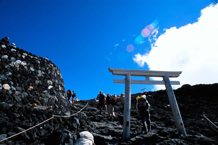 A rocky mountain path with hikers, a wooden signpost, and a clear blue sky. 1