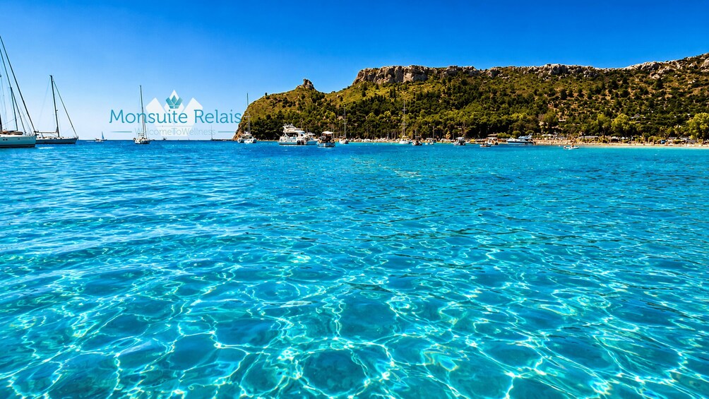 Clear turquoise sea, sailboats, and a coastal landscape with greenery. 4
