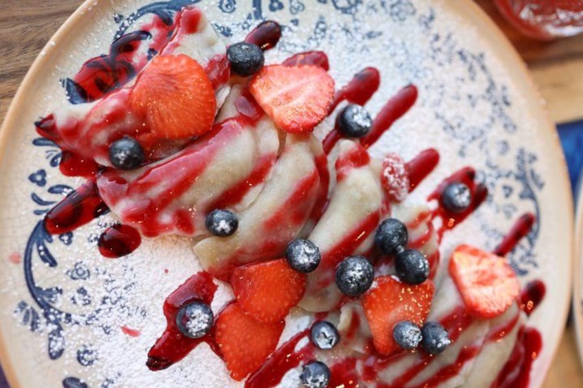 Una porción de panqueques cubiertos con fresas, arándanos y un almíbar rojo. 3