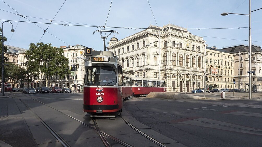 Punainen raitiovaunu, jonka numero on 4029, kulkee kiskoilla ja ohittaa historiallisia rakennuksia. 2