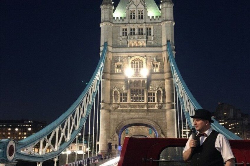 A person in a uniform standing in front of the Tower Bridge at night. 4