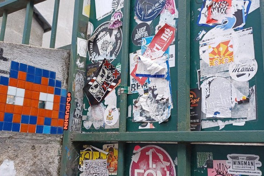 Una pared decorada con diversos adhesivos y carteles, incluyendo un patrón de mosaico azul y naranja a la izquierda. 4