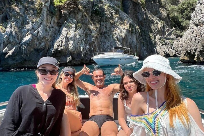 Un grupo de personas en un bote, con acantilados rocosos y agua azul cristalina al fondo. 4