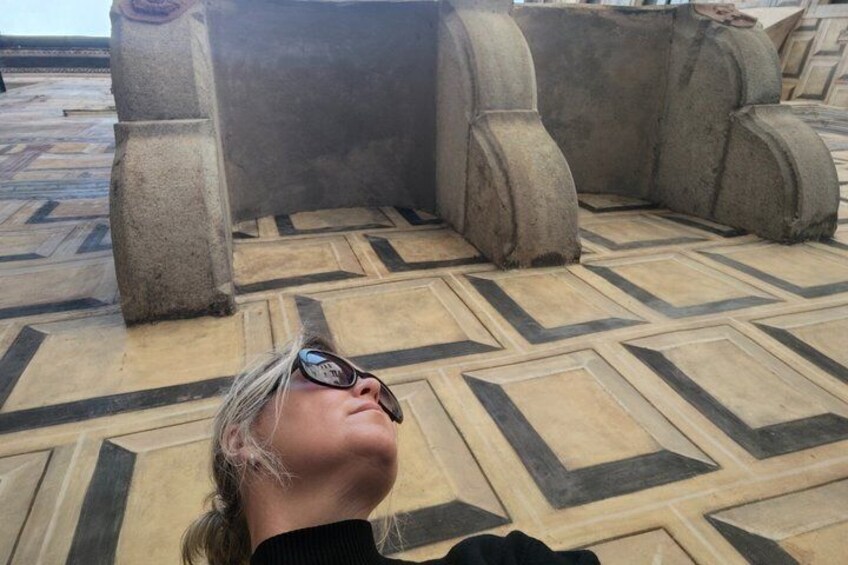 Una persona recostada sobre un piso estampado, con estructuras de piedra al fondo. 2
