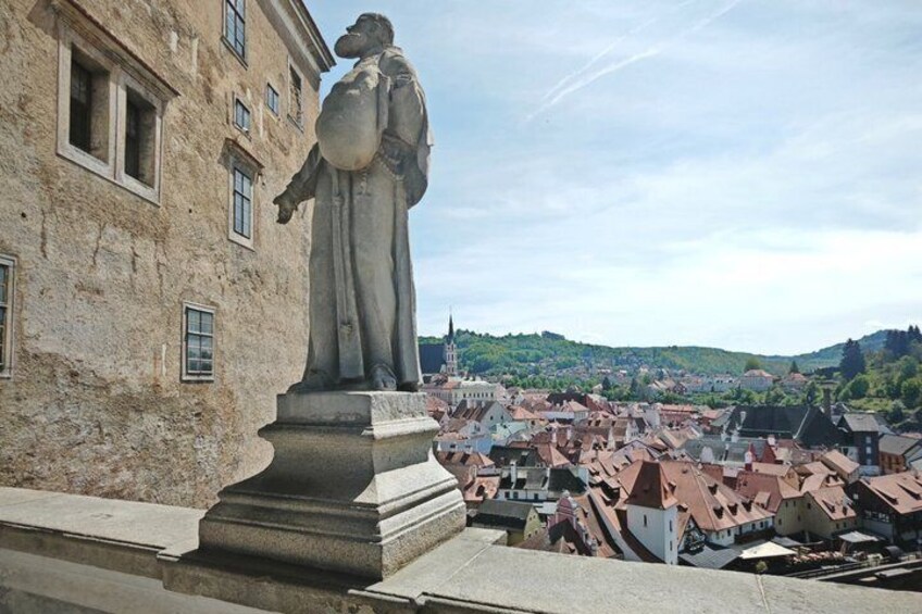 Una estatua sobre un pedestal, con vista a un pueblo de edificios con tejados rojos. 4