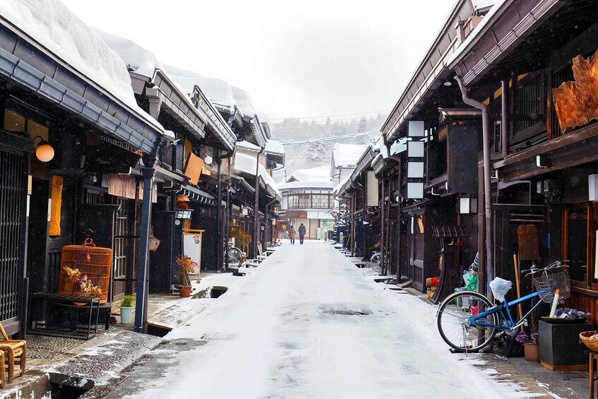 A snow-covered street with traditional buildings, a bicycle, and a birdcage. 4