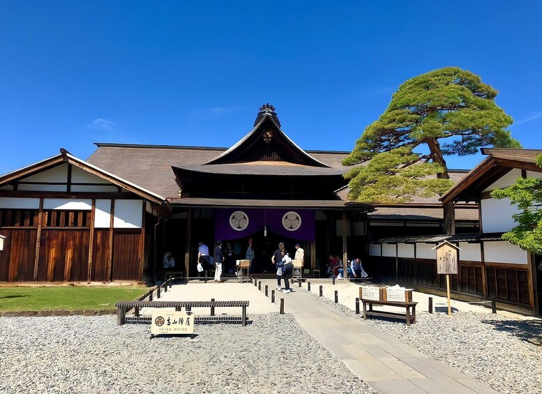 A traditional Japanese building with a wooden structure, a large tree, and a gravel pathway. 5