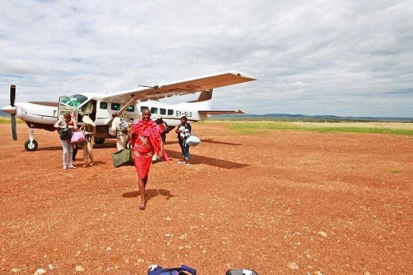 A small aircraft on a dirt runway with passengers boarding. 3
