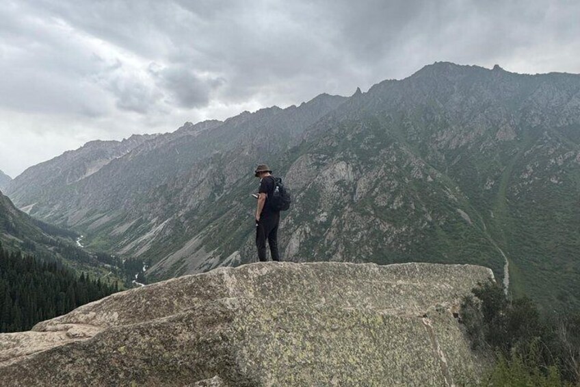A person standing on a rocky outcrop overlooking a mountainous landscape. 5