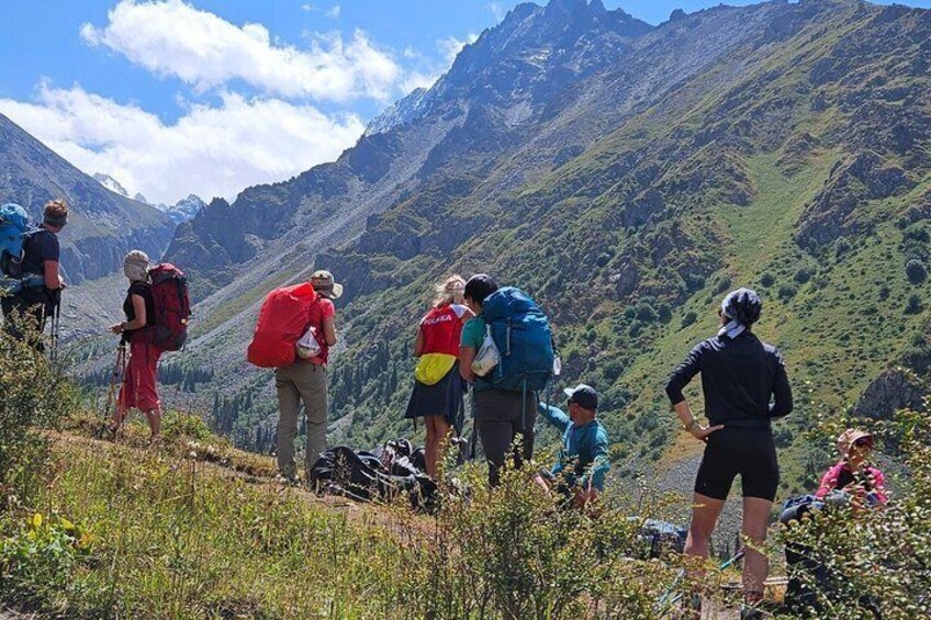 A group of hikers on a mountain trail with lush greenery and rugged terrain. 1