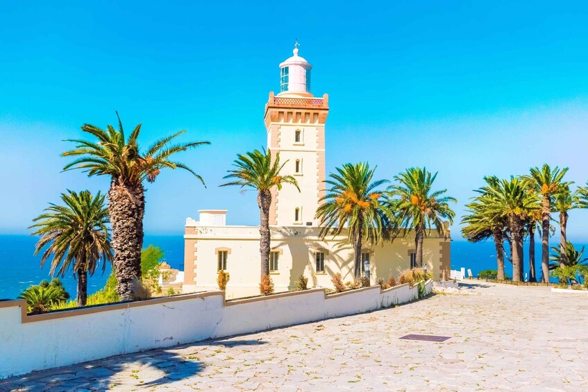 A coastal building with a lighthouse, palm trees, and the sea in the background. 1