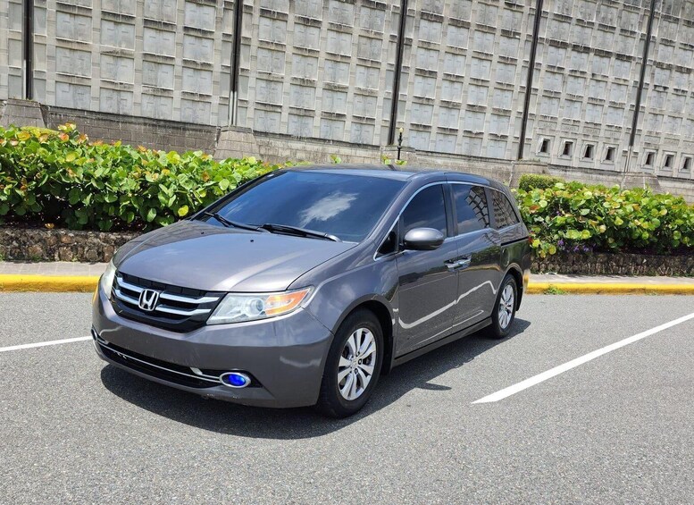 A gray Honda minivan parked in a lot with a stone wall and greenery in the background. 4