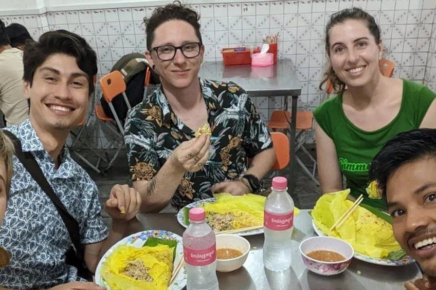 Cuatro personas sentadas a una mesa con comida, una botella de agua y un vaso rojo. 2