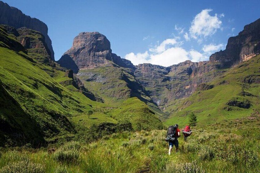 A hiker with a backpack walking through a grassy valley with mountains in the background. 1