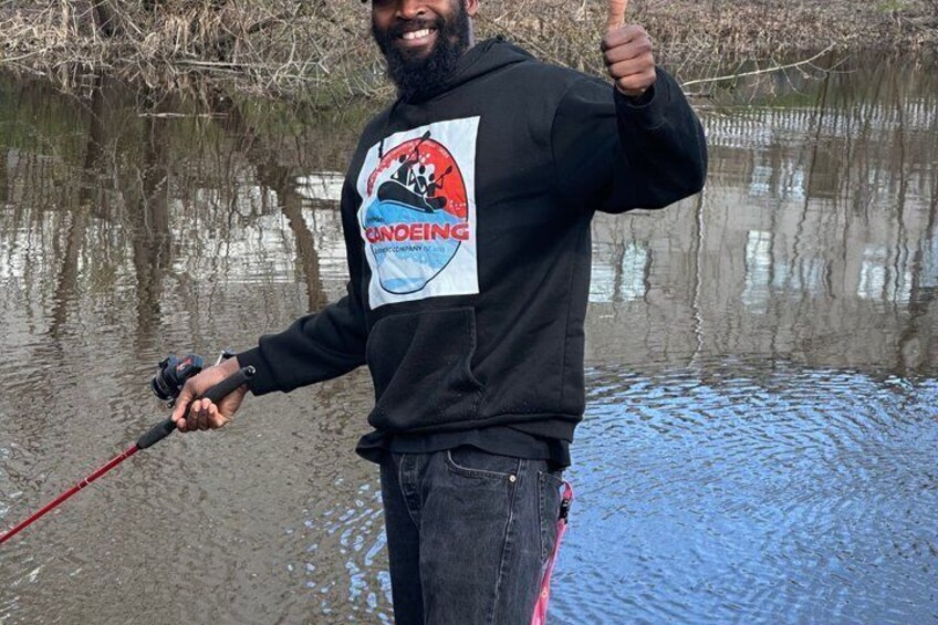 A person fishing by a calm body of water, wearing a black hoodie with a logo. 5