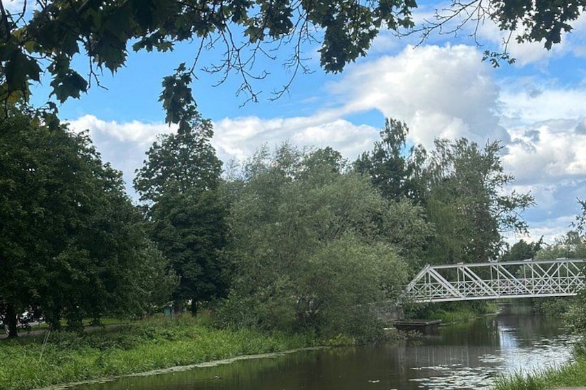 A river, a metal bridge, and dense trees under a partly cloudy sky. 2