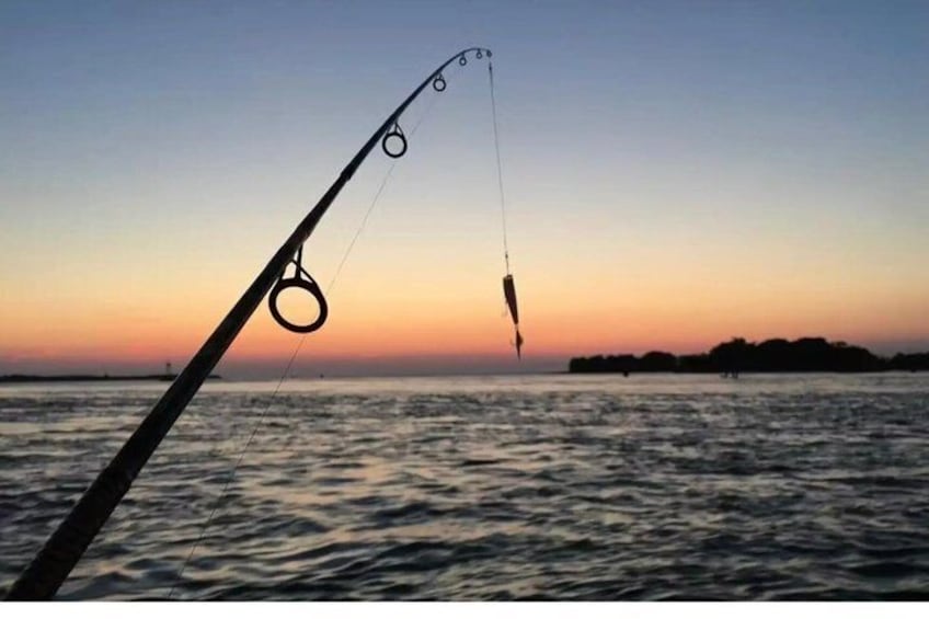 A fishing rod with a line extending into the water during sunset. 1