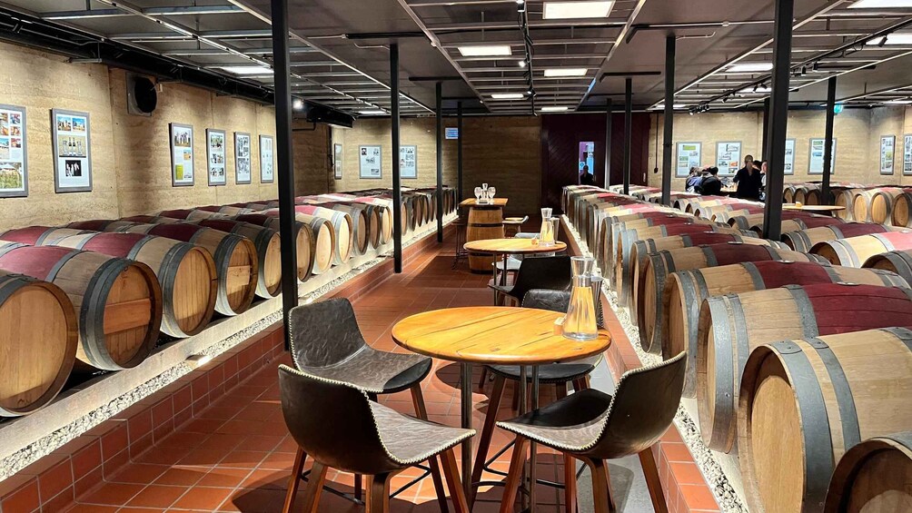 A wine cellar with rows of wooden barrels and tables with chairs. 2