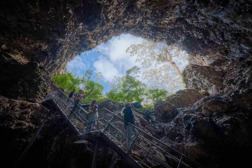 A cave entrance with a metal staircase leading inside, surrounded by rocky walls. 1