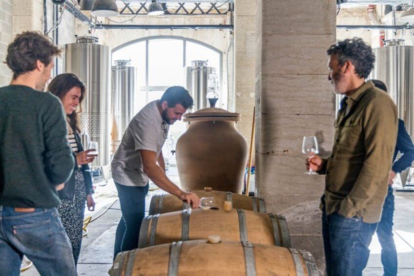 A group of people around a large wooden barrel, possibly in a winery or brewery setting. 1