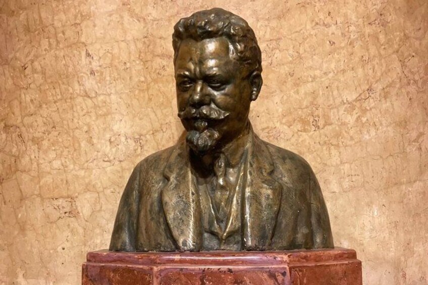 A bronze bust on a pedestal against a textured wall. 3
