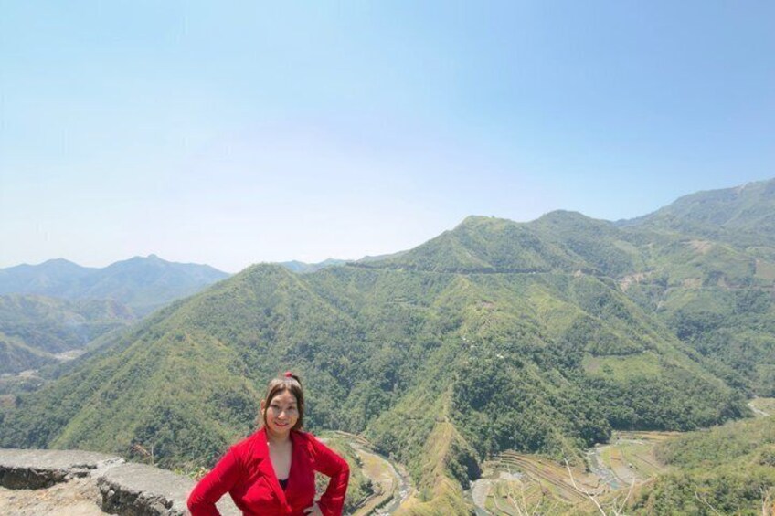 A person in a red jacket standing on a rocky outcrop with a mountainous landscape in the background. 2