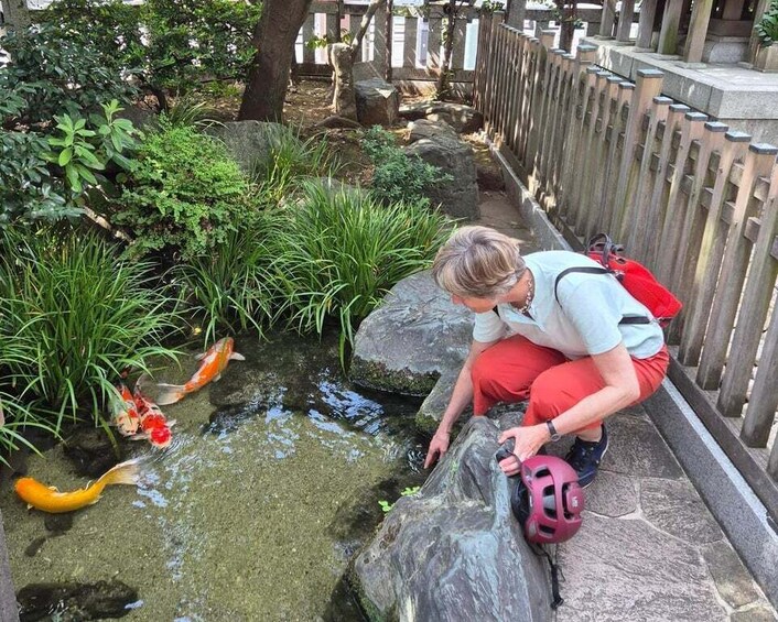 A person crouching by a koi pond with a helmet on the ground. 1
