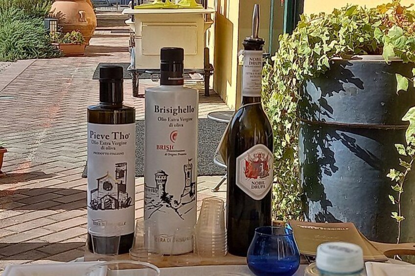 Three bottles of olive oil, a blue glass, and a metal container on a table. 3