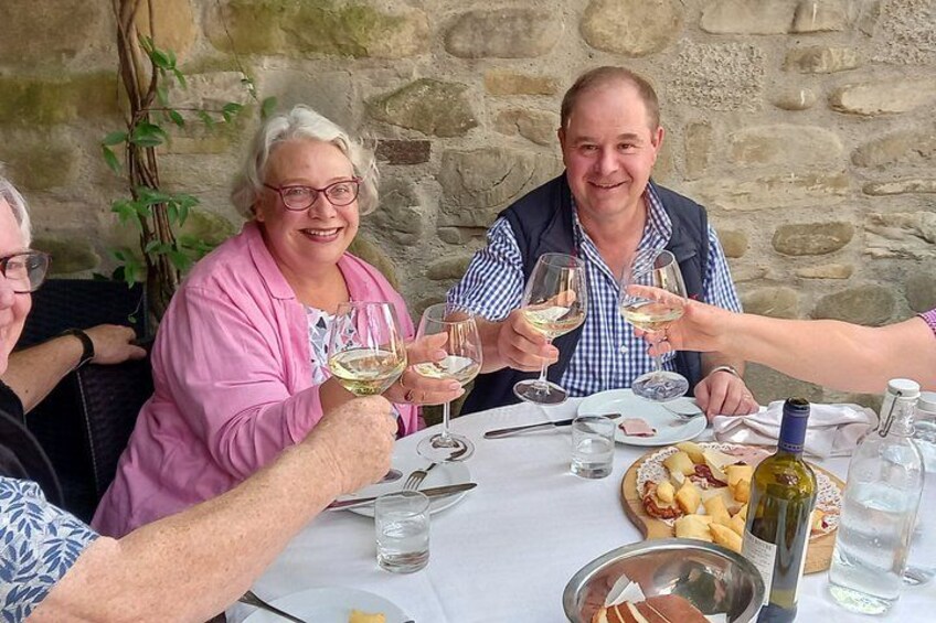 A group of people toasting with wine glasses at a table with food and a bottle of wine. 5