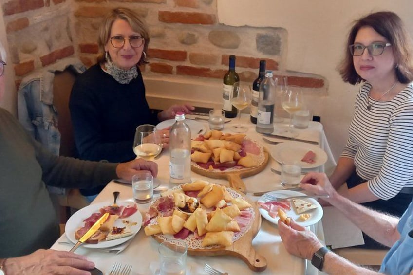 A group of people dining at a table with various dishes and wine bottles. 2