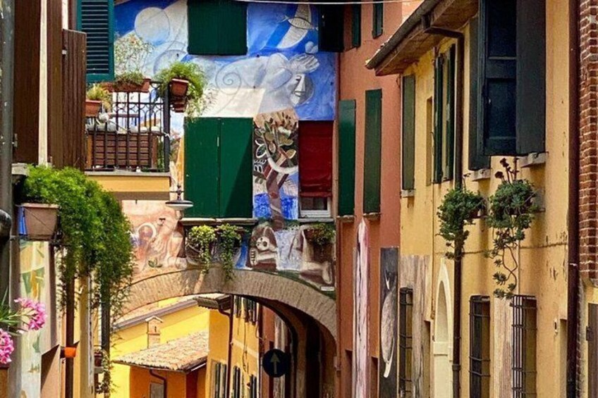 A narrow street with colorful buildings, a mural, and hanging plants. 1