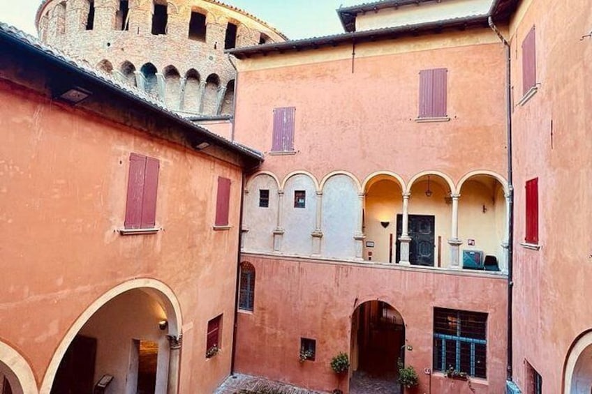 A courtyard with arches, a tower, and buildings with red shutters. 5