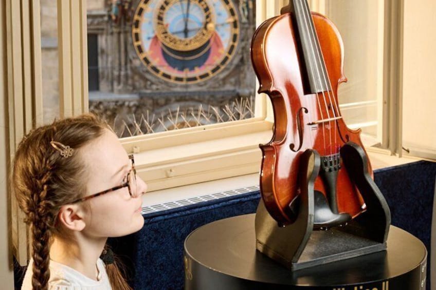 A violin on a stand in front of a window with a decorative wall piece. 1