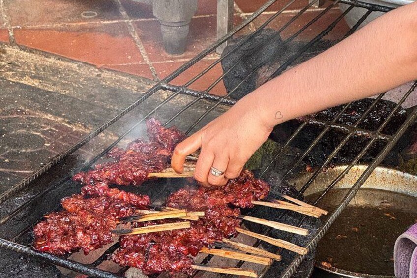 A person grilling meat on a barbecue over an open flame. 2