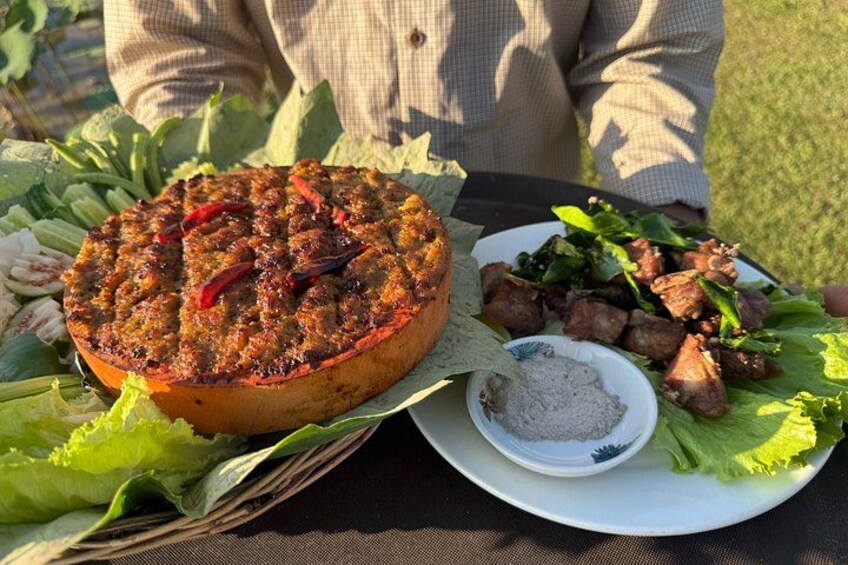 A meal with a large round dish, a plate with meat and greens, and a small bowl of sauce. 1