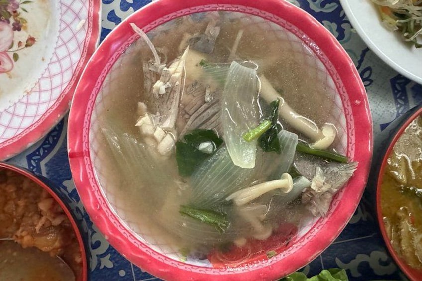 A bowl of soup with green vegetables and mushrooms, surrounded by other dishes. 5