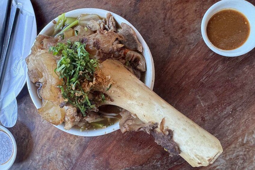 A bowl of soup with a large bone, meat, and green garnish. 3