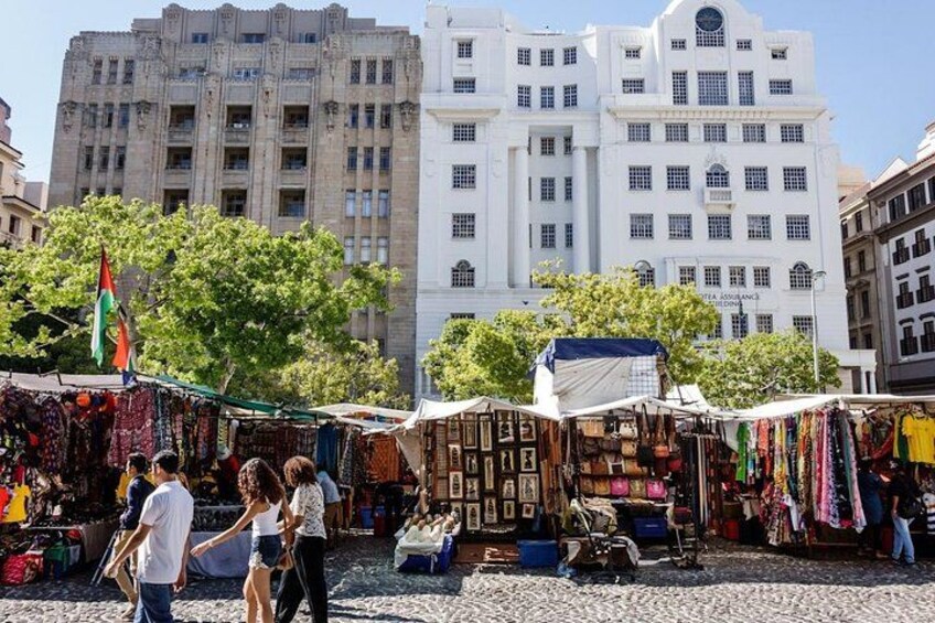 A bustling outdoor market with various stalls selling textiles and clothing, set against a backdrop of historic buildings. 2