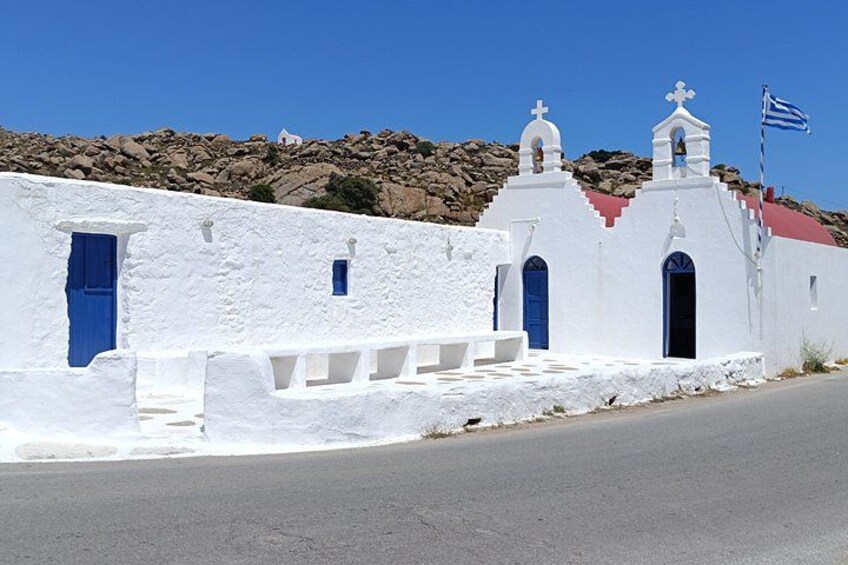 Una iglesia blanca con puertas azules y una bandera, frente a una ladera rocosa. 1