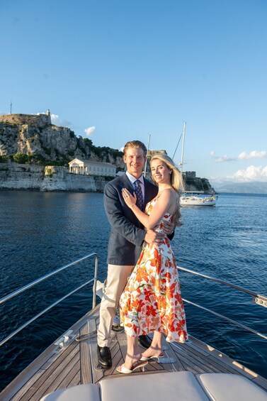 A couple embracing on a boat with a rocky coastline and a lighthouse in the background. 2