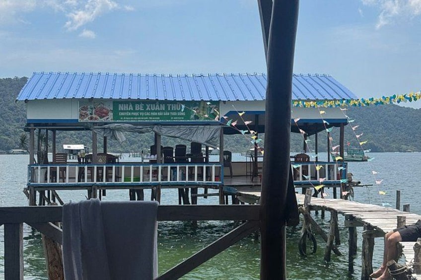 A floating restaurant with a blue roof and a signboard, surrounded by water and greenery. 3