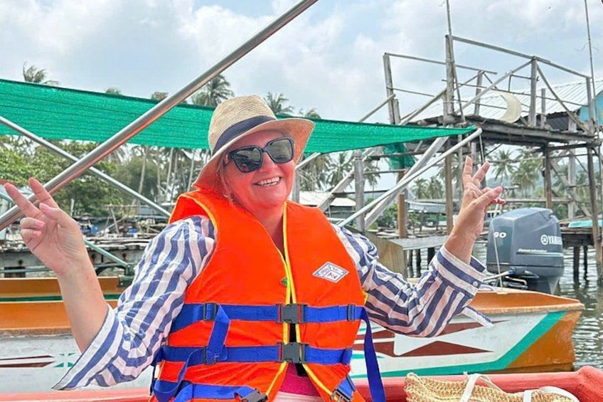 A person in a boat wearing a life jacket, with a motorboat and a dock in the background. 5