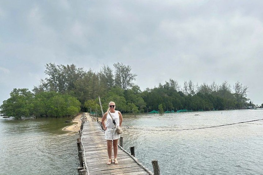 A person standing on a wooden bridge over calm water, surrounded by trees and a cloudy sky. 2