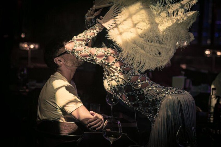 A person in a feathered, ornate costume interacting with another individual in a dimly lit setting. 3