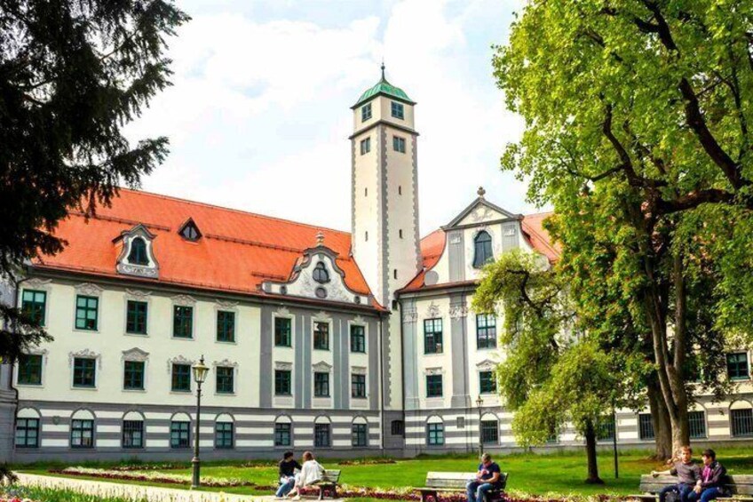 A historic building with a tower, surrounded by a well-maintained garden and a few people sitting on benches. 3