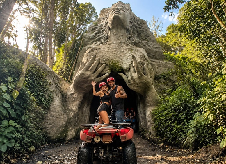 Eine große Felsformation mit Gesichtszügen, ein roter ATV und zwei Personen mit Helmen. 1