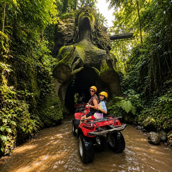 A red ATV navigating a narrow water channel surrounded by dense green foliage. 5