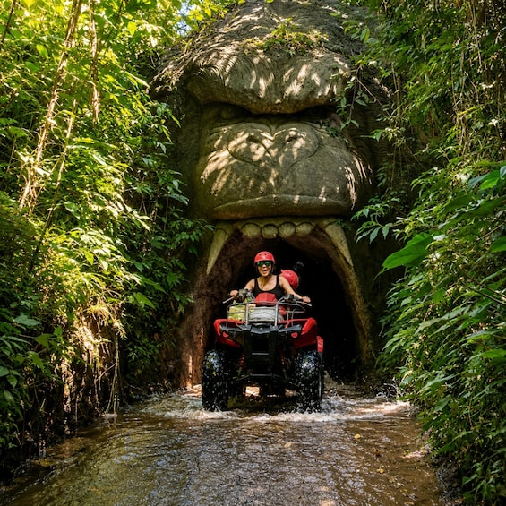 A person riding an ATV through a narrow water channel surrounded by dense foliage. 1