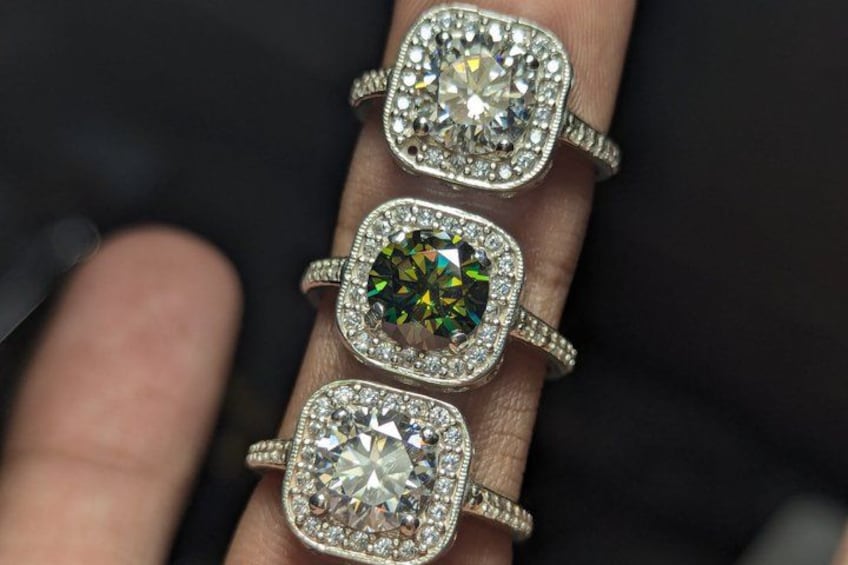 Een hand met drie vierkante diamantenringen, waarvan de middelste een groene edelsteen is. 4